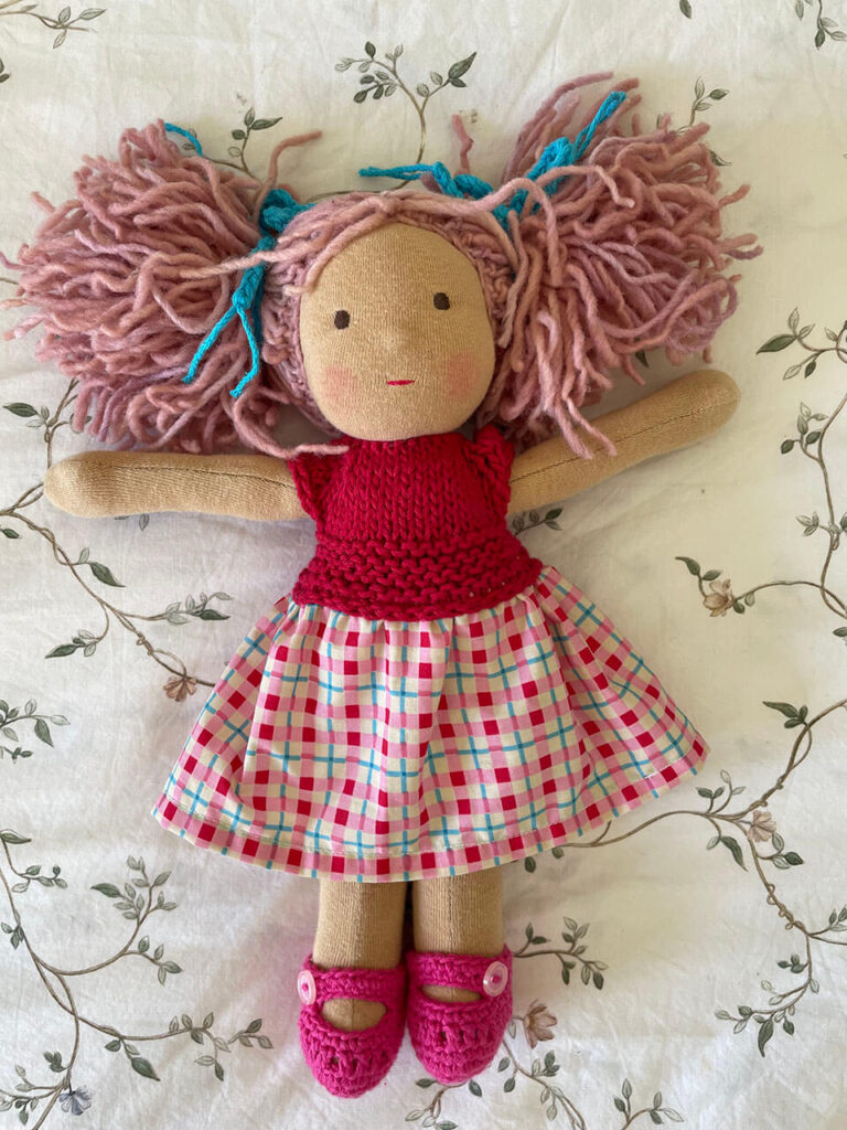 Muñeca pequeña con pelo color rosa claro y vestido tejido color rosa